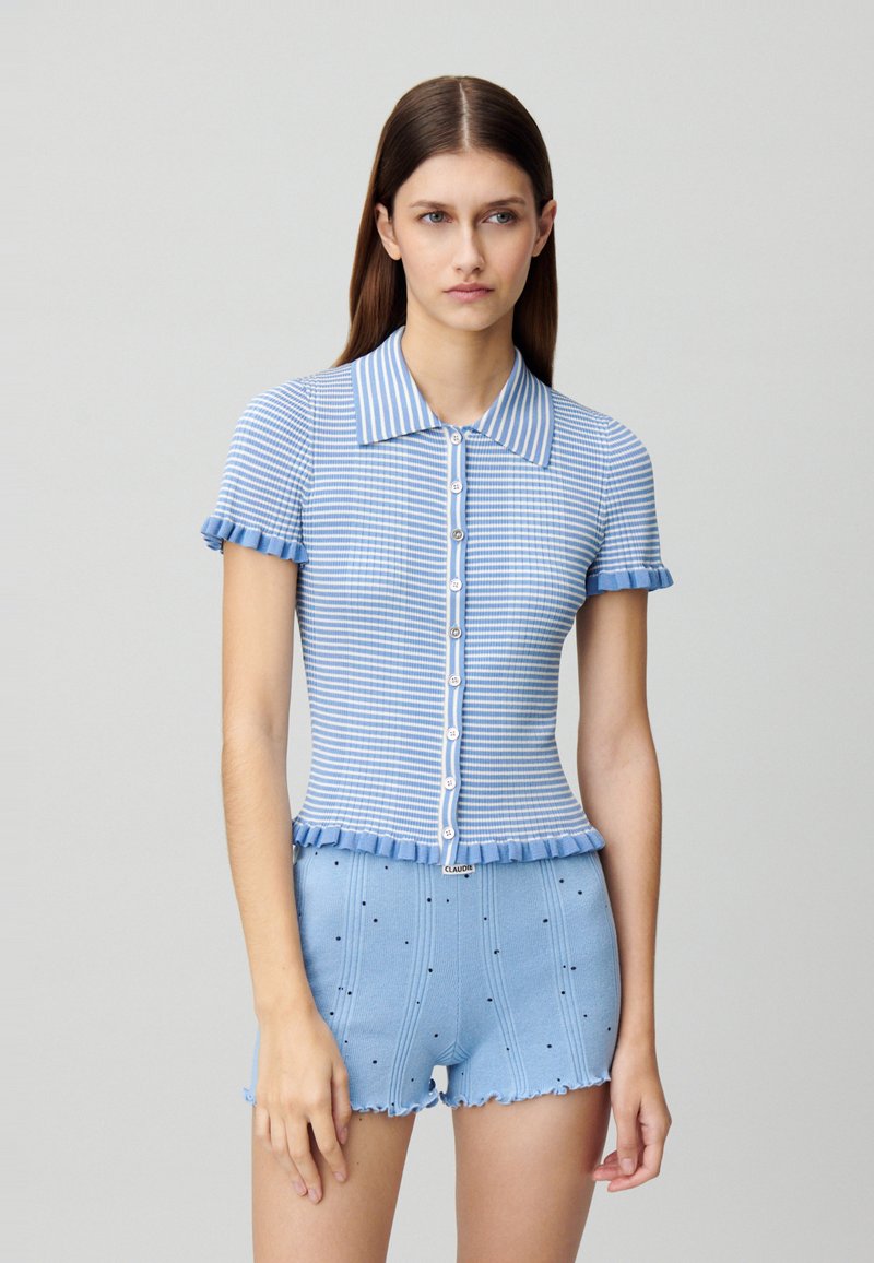 Top de punto a rayas azul y blanca con mangas cortas acampanadas, con un cierre de botones en la parte frontal. Combinado con pantalones cortos azules a juego con detalles decorativos.