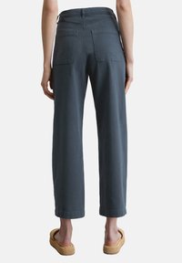 Grijze wijde broek met hoge taille, voorzien van twee achterzakken en een gladde, gestructureerde stof. Gepaard met gevlochten sandalen.