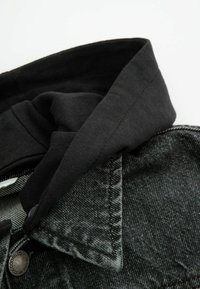 Czarna, kapturowa tkanina nałożona na szary dżinsowy kurtkę, z zapięciem na guziki i widocznymi detalami szwów. Teksturowana i strukturalna.