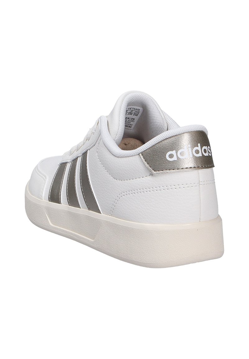 Sneaker blanche avec accents argentés, présentant trois rayures sur le côté, en cuir texturé et avec un intérieur rembourré. Branding notable sur le talon.
