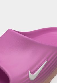 Detaljan prikaz ljubičaste Nike natikače s bijelim logom u obliku kvačice i teksturiranim potplatom.