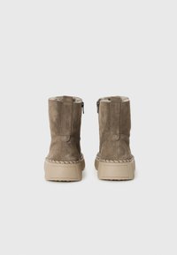 Stivali alla caviglia in suede color taupe con una morbida fodera, dotati di una suola testurizzata e un dettaglio intrecciato attorno alla base. Chiusura con zip sul retro.