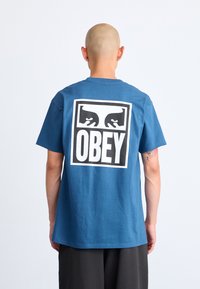 Blå bomull T-skjorte med en stor svart og hvit "OBEY" grafikk på baksiden, kort erm, og en avslappet passform.