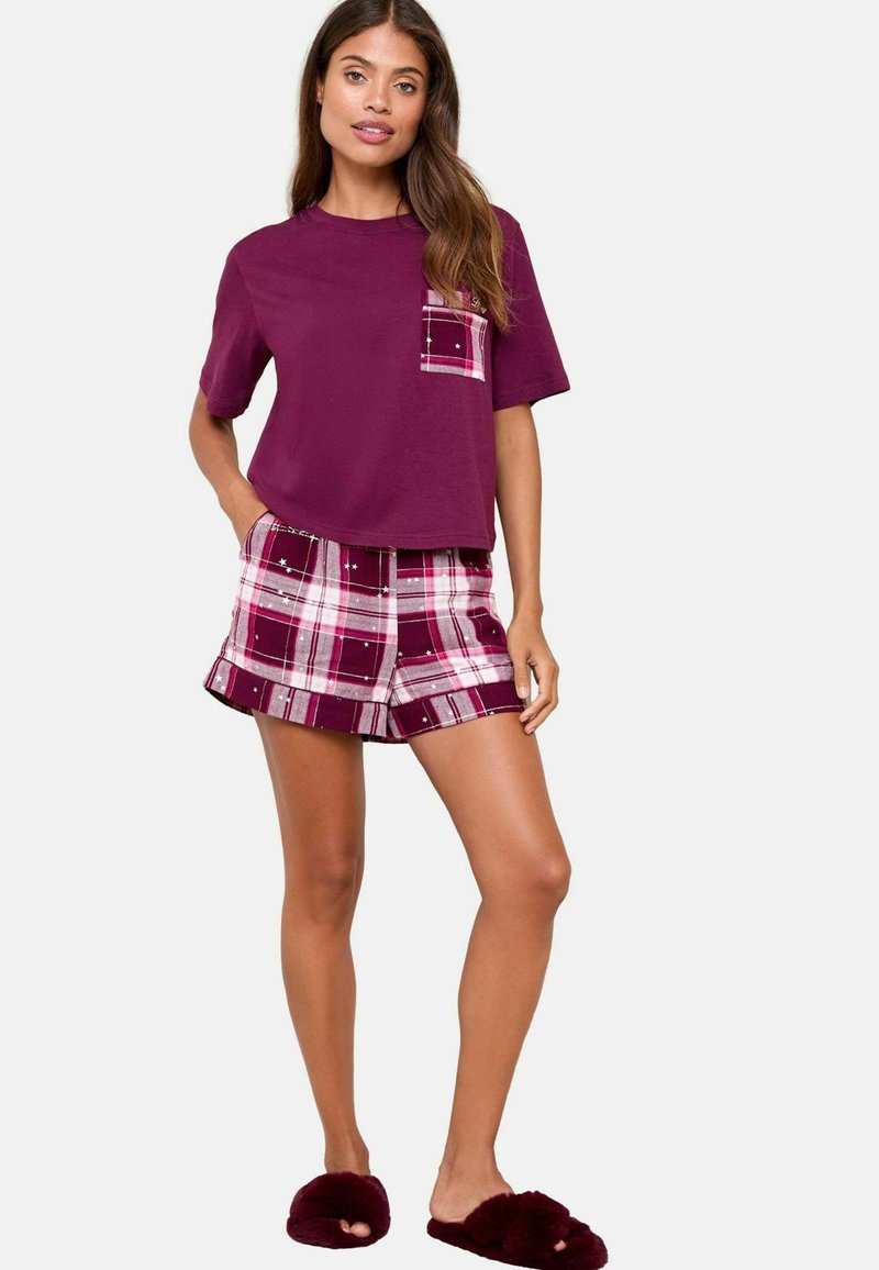 Lila pamut póló zsebbel, burgundi kockás nadrágra párosítva, fehér és rózsaszín vonalakkal. Puha, bolyhos burgundi papucs.