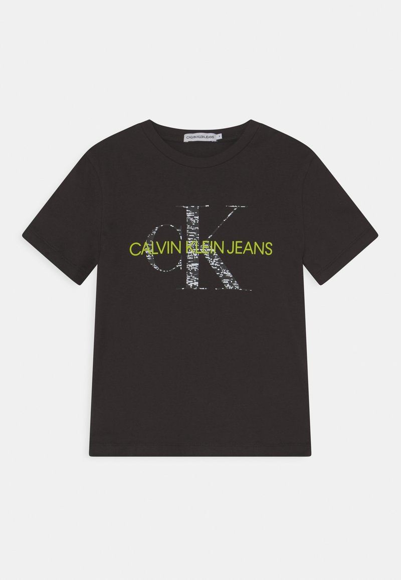 Černé bavlněné tričko s velkým, opotřebovaným bílým logem "CK" a textem "CALVIN KLEIN JEANS" v neonově zelené. Krátké rukávy a kulatý výstřih.