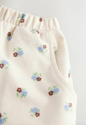 Tejido de color crema claro con una textura suave, que presenta un patrón floral de flores azules y burdeos. Cintura elástica y detalle de bolsillo lateral.