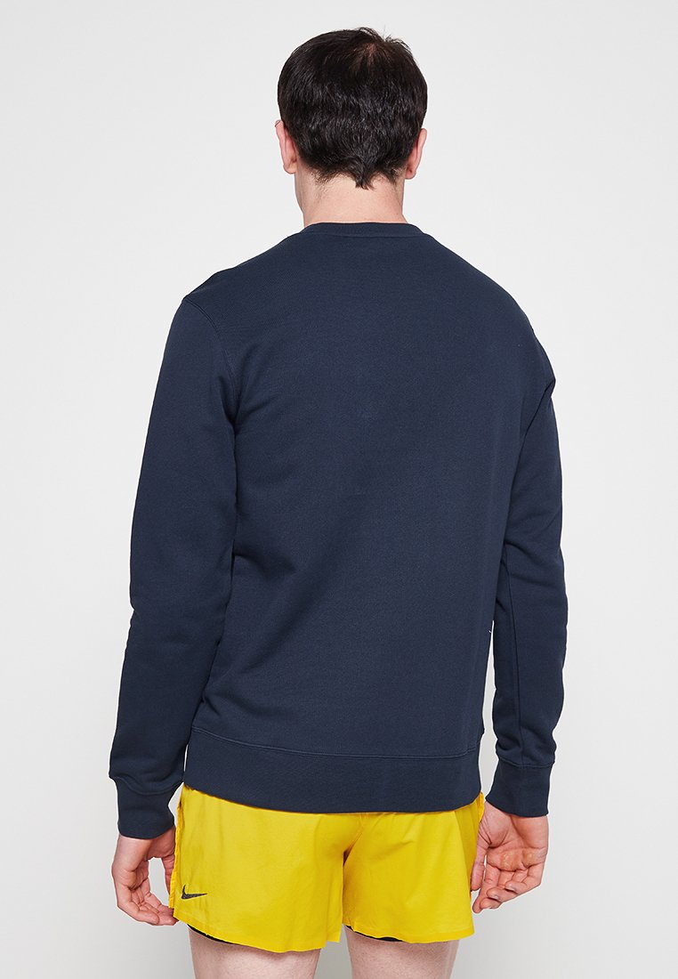 Navyblaues Sweatshirt aus weichem, strukturiertem Stoff mit Rundhalsausschnitt und langen Ärmeln, kombiniert mit gelben Shorts. Keine sichtbaren Logos oder Muster.