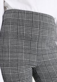 Mustat ja valkoiset houndstooth-kuvioiset housut, joissa on tummat valkoiset paidat, jotka on mahdutettu vyötärön ja yläreiden alueelle.