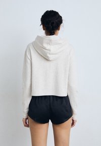 Moleton cropped cinza claro com capuz, feito de um tecido suave, combinado com calções pretos. O design apresenta linhas simples e limpas.