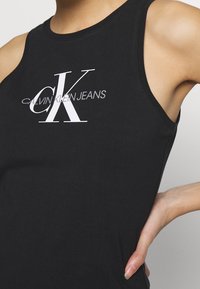 Czarna koszulka na ramiączkach z miękkiej bawełny, z okrągłym dekoltem. Posiada białe logo "CK" oraz napis "CALVIN KLEIN JEANS" poniżej w jasnoszarym kolorze.