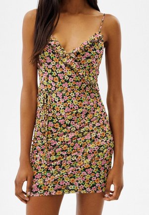 Blumiges Wickelkleid mit schwarzem Grund, das mit pinken und gelben Blumen verziert ist. Es hat verstellbare Spaghetti-Träger und ein Details mit Rüsche am Ausschnitt.