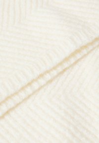 Bílá tkanina v herringbone vzoru, měkká textura, směs vlny, s jemným cik-cak vzorem a mírným leskem, který naznačuje kvalitní materiál.