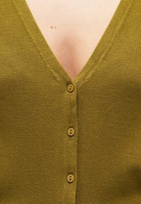 Cardigan vert olive avec un col en V, doté de quatre boutons ronds sur le devant et d'un tissu en maille doux et texturé.
