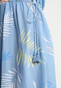 Tela azul con patrones de hojas tropicales en amarillo, blanco y rosa, con un cordón de ajuste con dos borlas atadas en la cintura.