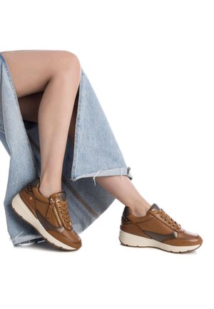 Zapatillas de cuero marrón con suelas crema, con un cierre lateral, texturas contrastantes y acentos metálicos. Combinadas con una falda de mezclilla clara.