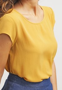 Blouse jaune à manches courtes en tissu léger, dotée d'un col rond et d'une coupe ample. Texture lisse avec un drapé subtil.