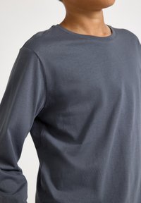 Långärmad t-shirt med rund halsringning, tillverkad av mjukt, mörkgrått tyg. Har en slät yta och avslappnad passform. Inga synliga mönster eller accenter.