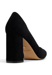 Escarpin noir en suede avec un talon bloc, un bout pointu et un accent en or sur la semelle. Texture lisse avec une finition mate.