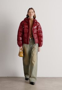 Puffete rød jakke med en skinnende finish, gulbrun genser, vide lysegrønne jeans og en liten gul håndveske. Outfiten har avslappede silhuetter.