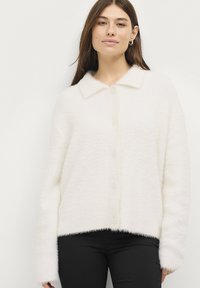 Witte donzige cardigan met een kraag, knopen aan de voorkant en lange mouwen, met een tekstuurstof en een cropped zoom. Gekocht over een zwarte broek.