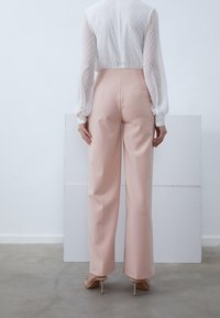 Pantalones de pierna ancha rosa claro con una textura suave, combinados con una blusa blanca transparente con lunares y mangas largas abullonadas.
