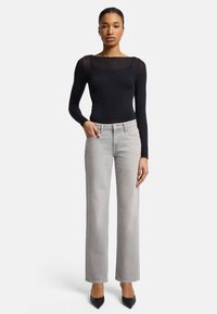 Black long-sleeve top with sheer fabric, paired with light gray wide-leg jeans. The outfit is complemented by black pointed-toe heels.
