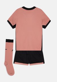 Camiseta deportiva rosa con acentos negros, combinada con pantalones cortos negros y un calcetín rosa. Hecha de un tejido transpirable con un acabado texturizado.