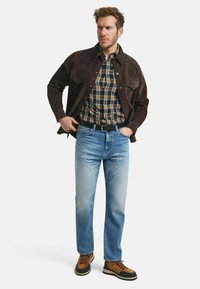 Bruine suède shirtjack over een geruit shirt. Lichte blauwe straight-leg jeans en bruine boots met zwarte rubberen zolen. Simpele, casual outfit.