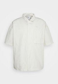 Bílá košile s krátkým rukávem vyrobená z bavlny, s designem na zapínání na knoflíky, jednou náprsní kapsou a vyšitým logem "AIR" na levé straně.