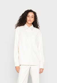 Camisa branca de botões com colarinho, mangas compridas e bolso no peito. Feita de um tecido liso com um corte relaxado.