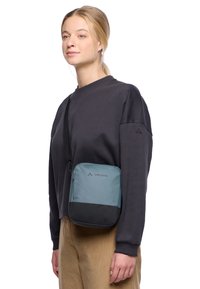 Piccolo crossbody in teal e nero, realizzato in tessuto texturizzato. Presenta una chiusura con zip superiore, logo e tracolla regolabile. Forma rettangolare.