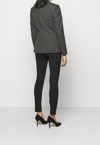 Grå skræddersyet blazer, sorte tætsiddende bukser og sorte højhælede sko, der fremhæver rene linjer og en elegant silhuet.