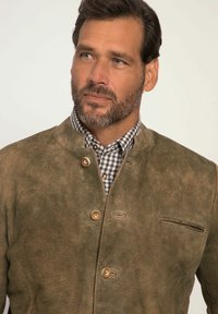 Bruine leren jas met een gestructureerde afwerking, voorzien van een staande kraag, houten knopen en een borstzak. Daaronder is een geruit shirt.