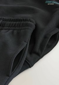 Schwarze Jogginghosen aus weichem Material, mit einem gerippten Bund, Seitentaschen und einem kleinen Logodetail auf der Vorderseite.