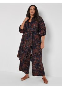 Fließendes, navy-blaues Kleid mit einem Blattmuster in Orange und Blau. Verfügt über Puffärmel, taillierten Bund und einen mehrlagigen Saum mit dekorativen Bändern.