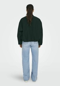 Zwarte oversized sweatshirt met elastische zoom, gecombineerd met lichtblauwe high-waisted wijde jeans, van achteren getoond.