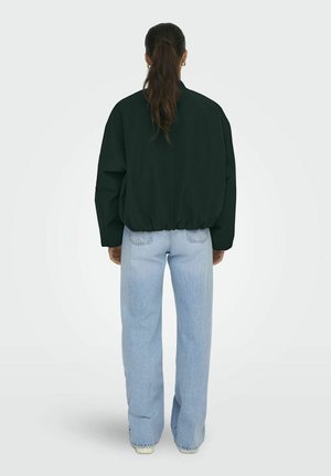 Schwarzes übergroßes Sweatshirt mit elastischem Saum, kombiniert mit hellblauen hochgeschnittenen weiten Jeans, von hinten betrachtet.