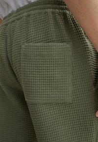 Olijfgroene, textuurdoek waffle-breisel shorts met een elastische tailleband en een opgestikte zak aan de rechterkant. Hoge duurzaamheid en casual ontwerp.