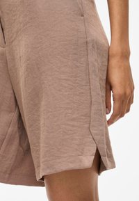 Abito in lino marrone chiaro con un'apertura laterale, tessuto testurizzato e orlo pulito. L'abito presenta una vestibilità rilassata con un design minimalista.