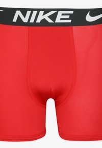 Rdeče atletske kratke hlače z črnim elastičnim pasom, ki ima bel logo 'NIKE' in udoben fit. Gladka tekstura z ravnimi šivi.
