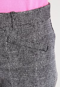 Black and white patterned trousers featuring a textured, woven design, with a contrasting patterned waistband and a side pocket detail.