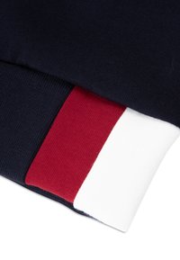 Felpa navy in tessuto con polsini a coste. I polsini presentano accenti rossi e bianchi. Tessuto liscio con un design aderente, che mostra colori sovrapposti.