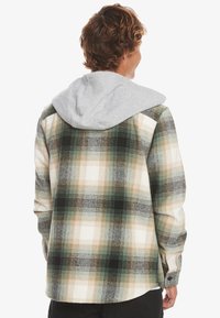 Rutigt flanellskjorta i beige, grön och svart, med en grå huva. Mjuk textur med knäppning och manschettdetaljer.