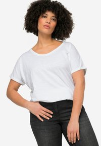 Losse witte katoenen t-shirt met opgerolde mouwen en een wijde hals, gecombineerd met donkere denim jeans. De textuur lijkt zacht en lichtgewicht.