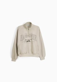 Beige pullover-tröja med halvdragkedja, med en stor "HANNOVER" grafisk design i svart, elastiska mudd och sidofickor.