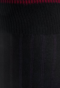 Leggings neri a coste con un tessuto testurizzato, dotati di una fascia rossa a contrasto nella parte superiore e sottili righe verticali su tutta la superficie.
