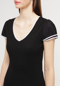 Black ribbed top with a deep V-neck and short puff sleeves. Features white accents on sleeve edges for contrast.