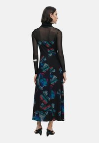 Abito nero floreale con orlo lungo, caratterizzato da una parte superiore trasparente e da motivi floreali astratti colorati in tonalità di blu, rosso e verde.