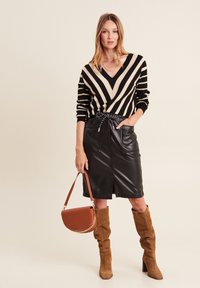 Schwarz-beige gestreifter Pullover mit V-Ausschnitt, kombiniert mit einem schwarzen Leder-Bleistiftrock, braunen Wildleder-Stiefeln bis zum Knie und einer braunen Handtasche.
