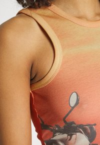 Ärmlös orange gradiente instoppad topp med ribbad halsringning och sidotryck av en motorcykel. Mjuk, åtsittande textur som visar en detaljerad design.